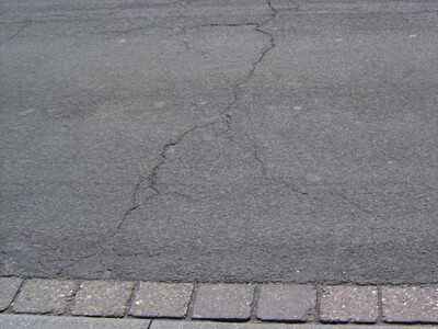 Das Bild zeigt die Rissbildungen durch Netzrisse und Flicken in der Asphaltdecke.